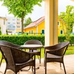 Terrasse mit Tisch und drei Stühlen. Blick auf grünen Rasen und Häuser im Hintergrund.