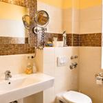Badezimmer mit Waschbecken, Toilette und Spiegel. Wandverkleidung mit Mosaikfliesen.