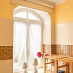 Badezimmer mit gelben Wänden, Holzregal und Fenster mit weißen Vorhängen.