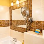 Badezimmer mit Waschbecken, Spiegel und Mosaikfliesen an den Wänden.