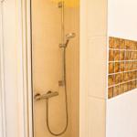 Dusche mit Duschbrause und Glaswand, Wand mit Mosaikfliesen.