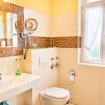 Badezimmer mit Waschbecken, Toilette und Dusche. Fenster mit weißen Vorhängen.