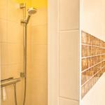 Dusche mit Duschbrause und Glaswand. Wand mit Mosaikfliesen.
