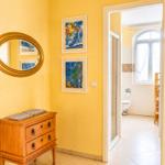 Helle Wand mit Spiegel, Schrank und zwei Bildern. Tür führt in Bad mit Toilette.