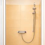 Dusche mit Handbrause und Temperaturregler an cremefarbenen Fliesen