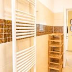 Flur mit Holzregal und Heizkörper, Wand mit Mosaikfliesen, Blick in die Küche.