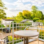 Terrasse mit Tisch und Stühlen, Vogelstatue auf Geländer, Blick auf Grünflächen und Hof.