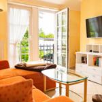 Wohnzimmer mit orangefarbenem Sofa, Glas-Tisch und Fernseher an der Wand.