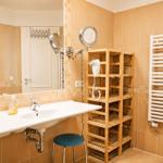 Badezimmer mit Waschbecken, Spiegel, Holzregal und Heizkörper.