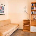 Ein Raum mit Sofa, Bücherregal und Wandbild mit Blumenmotiv.