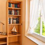 Bücherregal neben Fenster mit weißen Vorhängen und Segelschiffmodell