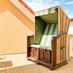 Terrasse mit Strandkorb, Tisch und Stühlen. Hintergrund: Wand und Himmel.