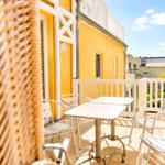 Terrasse mit Tisch und Stühlen vor gelbem Haus mit weißem Geländer.