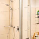 Dusche mit Glaswand, Duschbrause und Ablage mit Kosmetikartikeln.