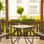 Terrasse mit Tisch und zwei Stühlen, Blick auf grünen Garten und Gebäude.