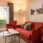 Ein Wohnzimmer mit rotem Sofa, Sitzgelegenheiten und Blick auf einen Balkon.