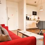 Wohnbereich mit rotem Sofa, Küchenbereich und Essplatz mit grauen Stühlen.