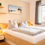Schlafzimmer mit Holzbett, Nachttisch und Wandbild. Fenster mit Vorhängen.