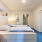 Schlafzimmer mit Doppelbett, Wandbild und Blick in angrenzenden Raum.
