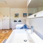 Badezimmer mit zwei Waschbecken, Spiegelschrank und Strandmotivbildern an der Wand.