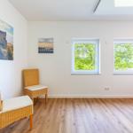 Zimmer mit zwei Fenstern, Holzboden und zwei Stühlen. Wandbilder und Bett sind sichtbar.
