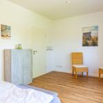 Schlafzimmer mit Bett, Kleiderschrank, zwei Stühlen und Wandbildern.