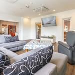 Wohnzimmer mit Sofa, Fernseher und Sessel. Tisch mit Tischdecke und Bilder an der Wand.