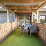 Terrasse mit Sitzgruppe, grünem Kunstgras und Holzüberdachung.