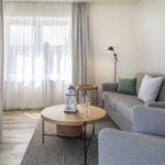 Ein Wohnzimmer mit grauem Sofa, runden Tisch und Fenster mit Vorhängen.