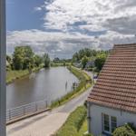 Aus dem Fenster blickt man auf einen Kanal mit Uferweg und Häusern unter bewölktem Himmel.