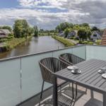 Terrasse mit Tisch und Stühlen, Blick auf einen Kanal und Wohnhäuser.