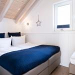 Schlafzimmer mit Doppelbett und kleinem Bett, Holzdecke und Fenster mit Jalousien.