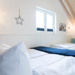 Zwei Betten mit weißen Laken und blauen Decken unter einem Holzdach