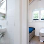 Badezimmer mit Waschbecken und Spiegel. Nebenraum mit zwei Betten und Fenster.