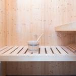 Sauna mit Holzbank, Eimer und Besen. Holzwände und -boden.
