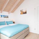 Schlafzimmer mit Bett, Holzdecke und Wandbild. Tür und TV sichtbar.