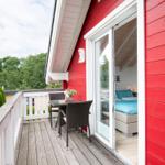 Roter Holzausbau mit Terrasse und Blick in Schlafzimmer mit blauer Bettwäsche.