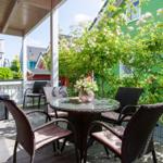 Terrasse mit Tisch und Stühlen, umgeben von grünen Pflanzen und einem grünen Haus.