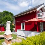 Rotes Haus mit Balkon, Terrasse und Garten. Roter Sonnenschirm und Grillplatz.