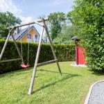Hinterhof mit Schaukel, Rasenfläche und rotem Gartenhaus. Im Hintergrund ist ein Haus mit Solaranlage zu sehen.