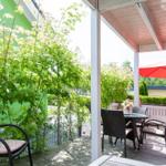 Terrasse mit Tisch, Stühlen und rotem Sonnenschirm. Grün bewachsene Wand im Hintergrund.