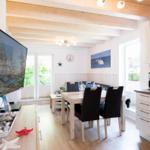 Wohn- und Essbereich mit TV, Esstisch und Küchenzeile. Holzdeckenbalken und Fenster mit Blick.