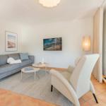 Wohnzimmer mit Sofa, Sessel, Couchtisch und Fernseher an der Wand.