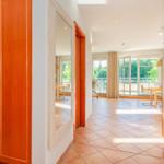 Flur mit Holzschrank, Spiegel und Blick in Wohnbereich mit Terrasse.