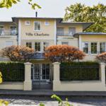 Villa Charlotte mit Eingangstor, Hecke und Bäumen im Herbst.