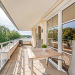 Terrasse mit Tisch, Stühlen und Blick auf grüne Bäume.
