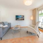 Wohnzimmer mit Sofa, Sessel, Couchtisch und Fernseher. Durchgang zur Terrasse mit Blick auf Garten.