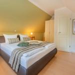 Schlafzimmer mit Doppelbett, Nachttischen, Kleiderschrank und Sessel.