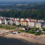 Strand mit Steg und bunten Strandkörben vor historischen Häusern am Wasser.