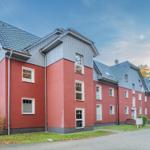 Rotes Mehrfamilienhaus mit grauem Dach und weißen Fenstern.